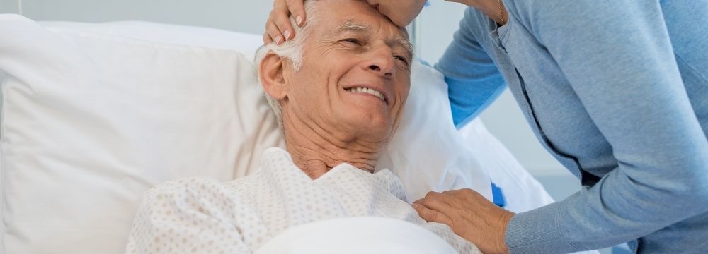Old man in hospital bed recovering from a cardiac catheter ablation with family member by his side