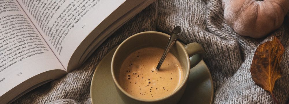 Coffee cup on bed with book and fake pumpkin