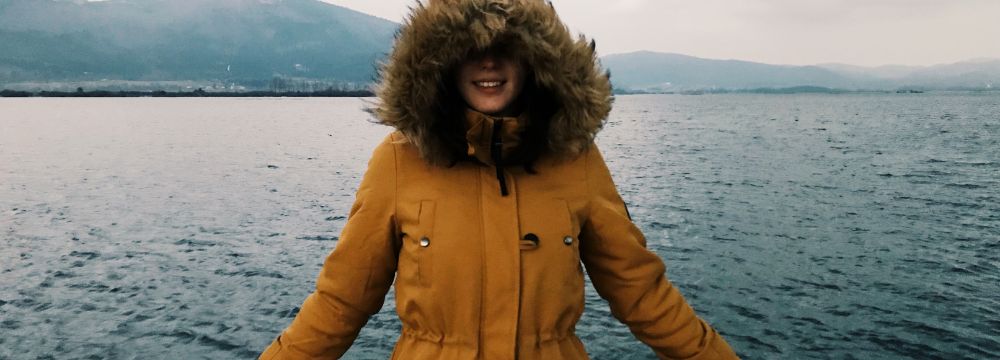 Woman standing leaning on rail in winter parka coat by a body of water