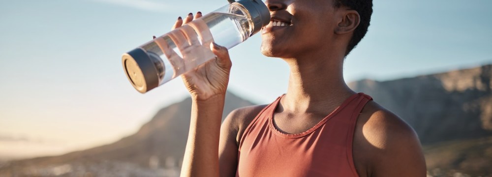 Woman smiling while sipping water out of clear bottle 